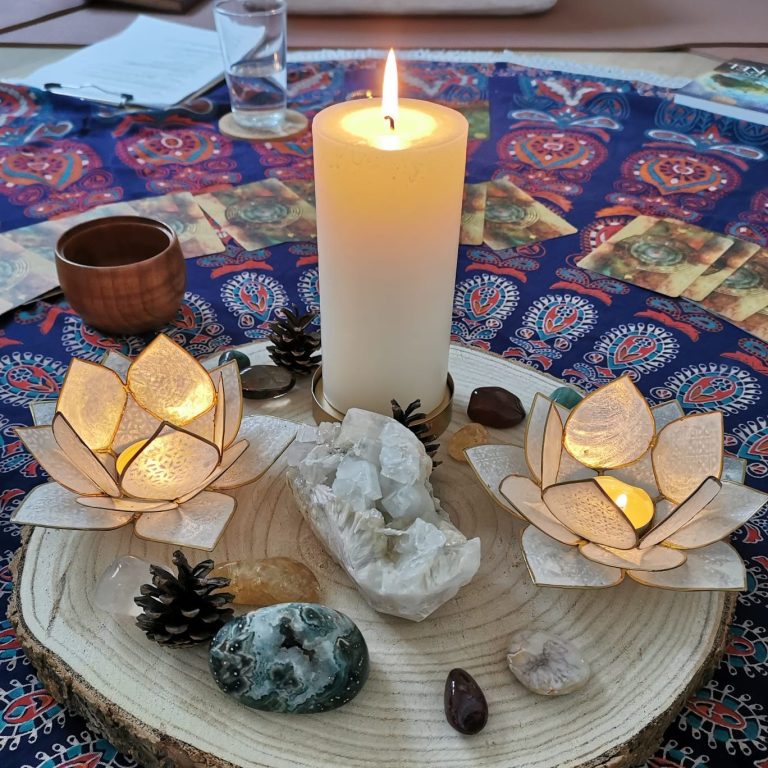 Bunter Teppich mit Kerzen, Kristallen, Orakelkarten und dekorativem Holzstück in der Mitte.